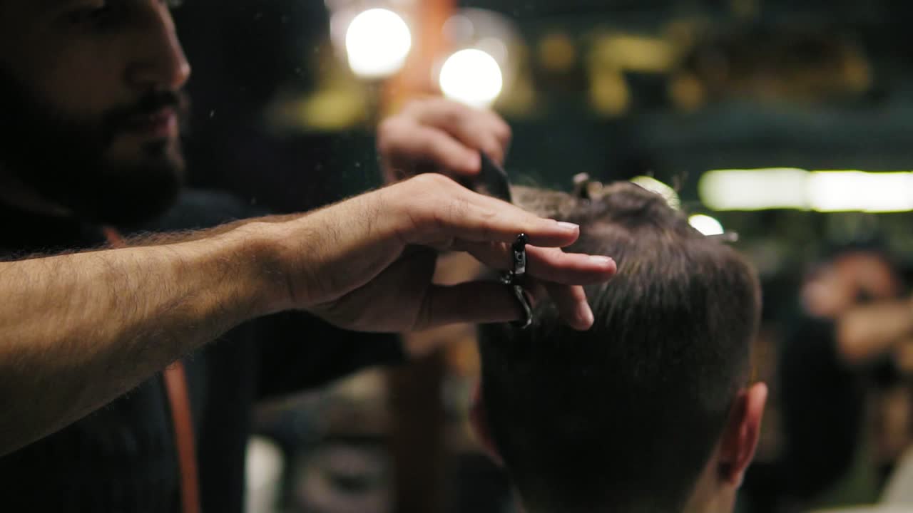 Close Up view of the barber's hands performing a haircut with scissors and combing the client. Slow Motion shot