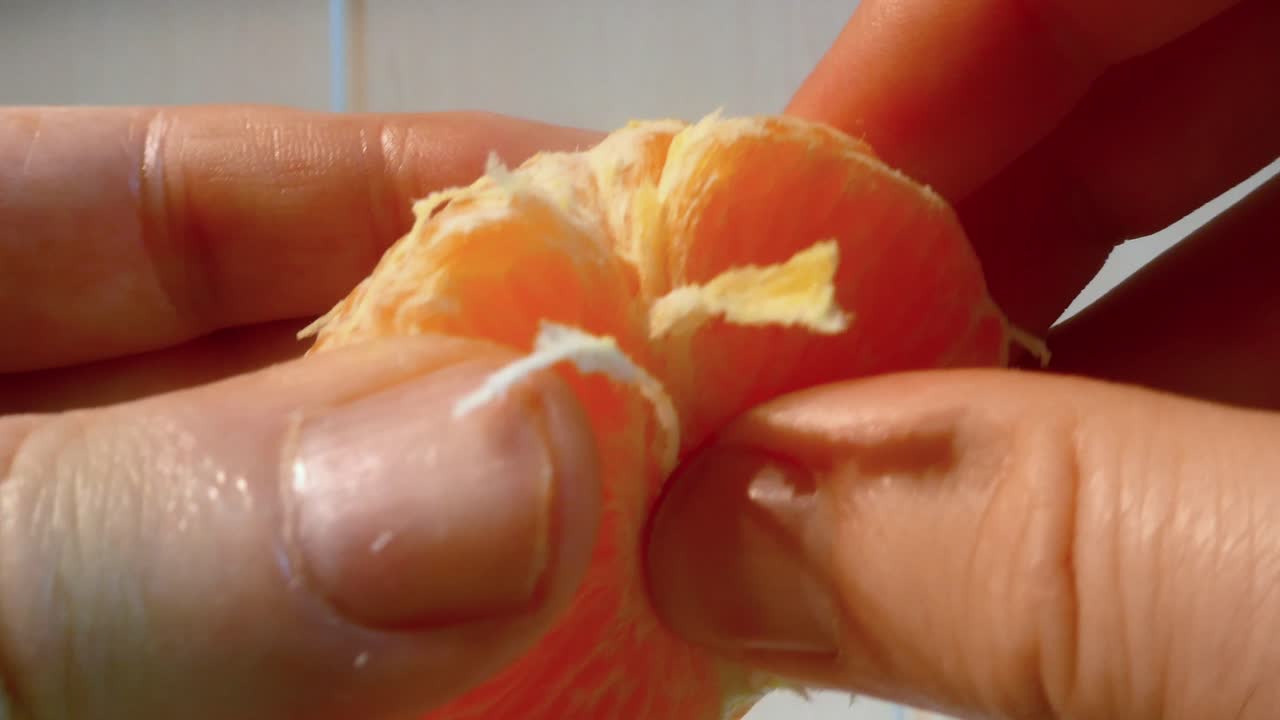 Vista de cerca de manos separando cuidadosamente los gajos de una mandarina fresca y jugosa