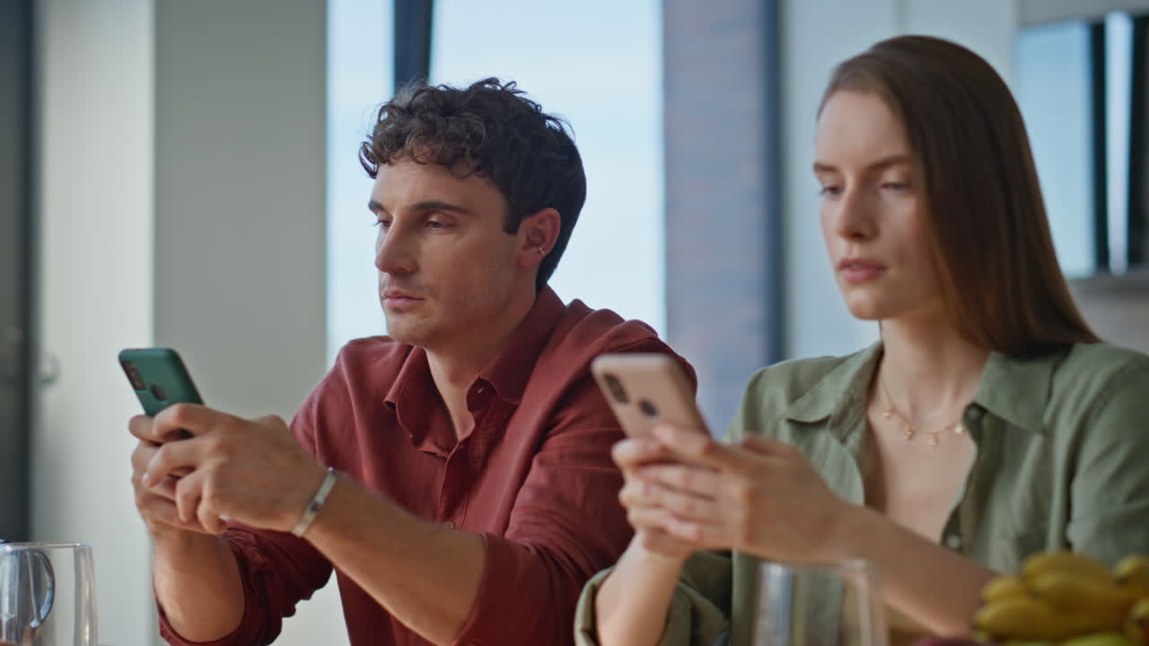 Focused family addicted gadgets sitting at breakfast using smartphones closeup