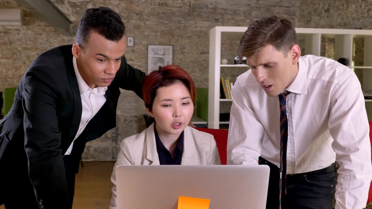 스 인종의 세 명의 사업가들이 노트북을 통해 현대적인 사무실에서 프로젝트와 계획에 대해 논의하고 있습니다.