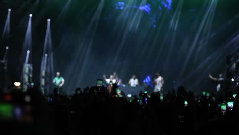 artists singing and dancing on stage, fans recording video with smart phones at music concert