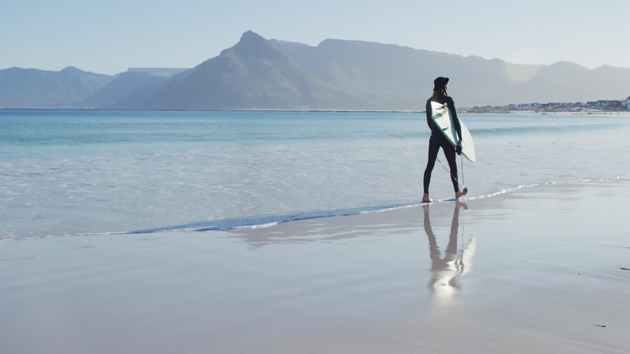 ⁇ 은 해변에서 서핑 보드를 들고 다니는 웨이트스 ⁇ 을 입은 백인 남자의 비디오