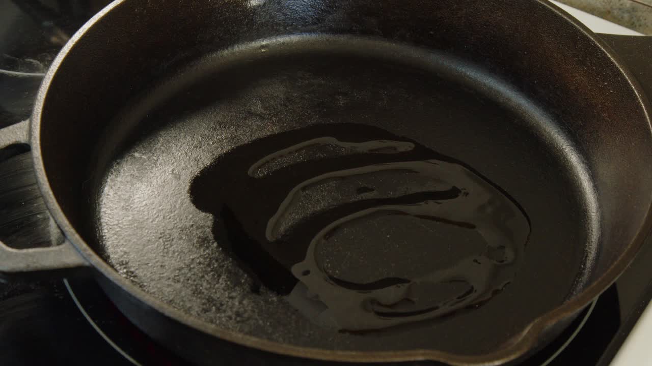 Closeup oil is poured into hot cast iron pan on stove top