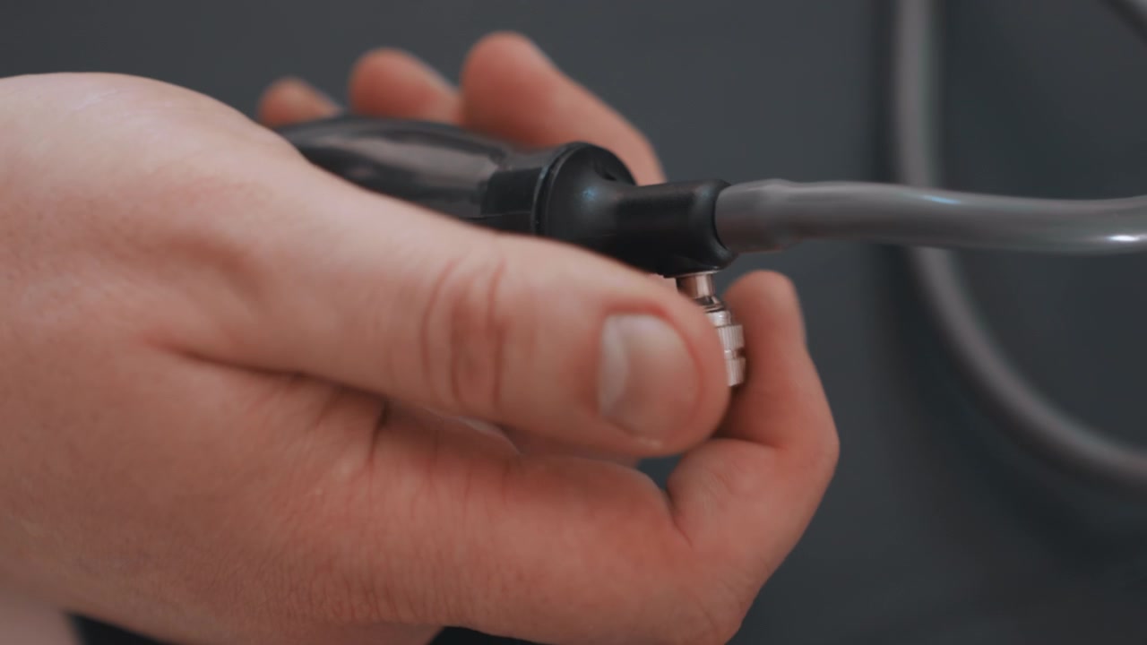 Closeup white paramedic hand connecting metal fitting to black inflation tube, precise coupling motion, portable monitor prep in tense roadside ambulance environment, focus on connector and secure