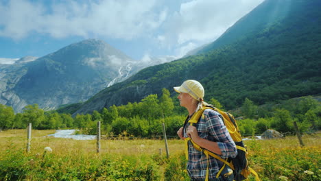 An-Active-Woman-With-A-Backpack-Walks-Against-The-Backdrop-Of-The-Mountains-And-The-Briksdal-Glacier