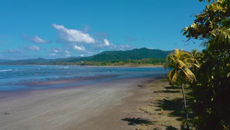 a perfect empty beach with long waves rolling on the shore at the pacific ocean in costa rica on a nice sunny day filmed from above with a drone.