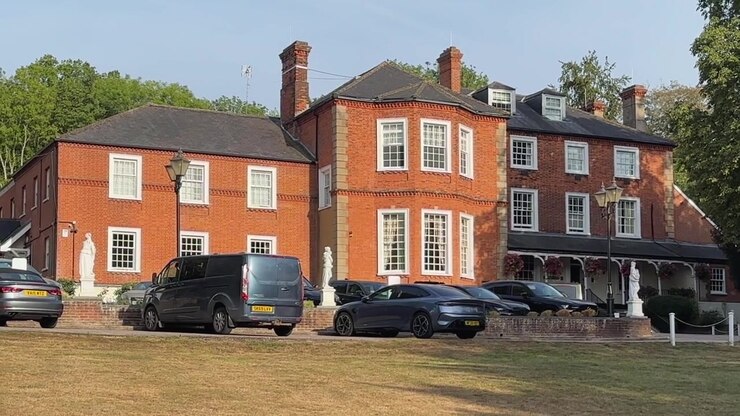 L'hotel e spa Brandshatch Place, in mattoni rossi, con finestre bianche e auto parcheggiate, si affaccia su un prato estivo secco