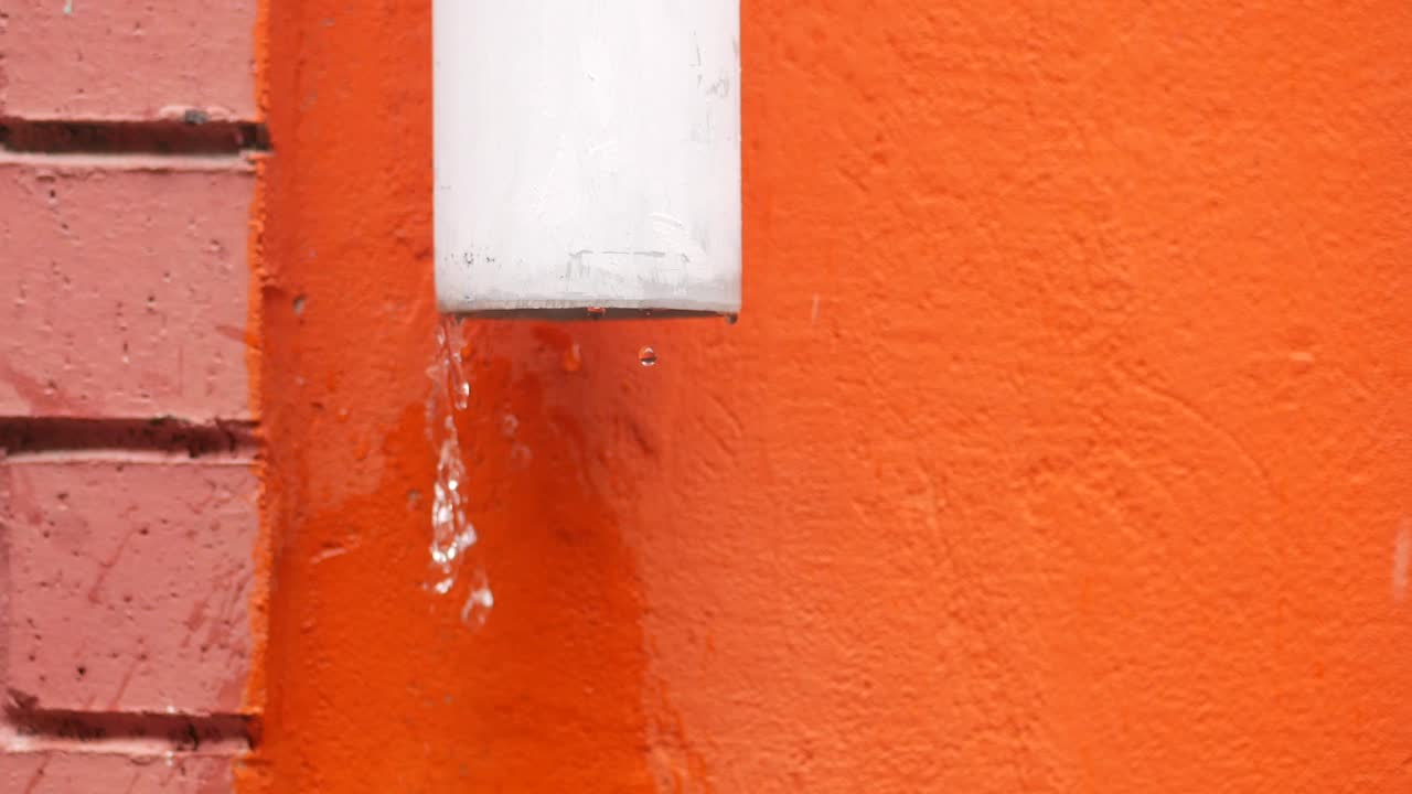 Water dripping from a rain gutter on an orange wall