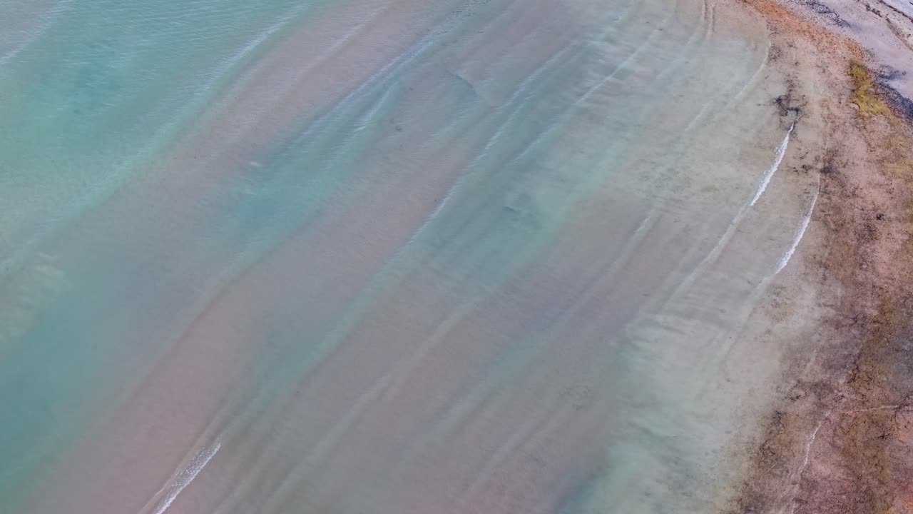 Aerial drone view of a serene turquoise shoreline with gentle waves lapping against a sandy beach