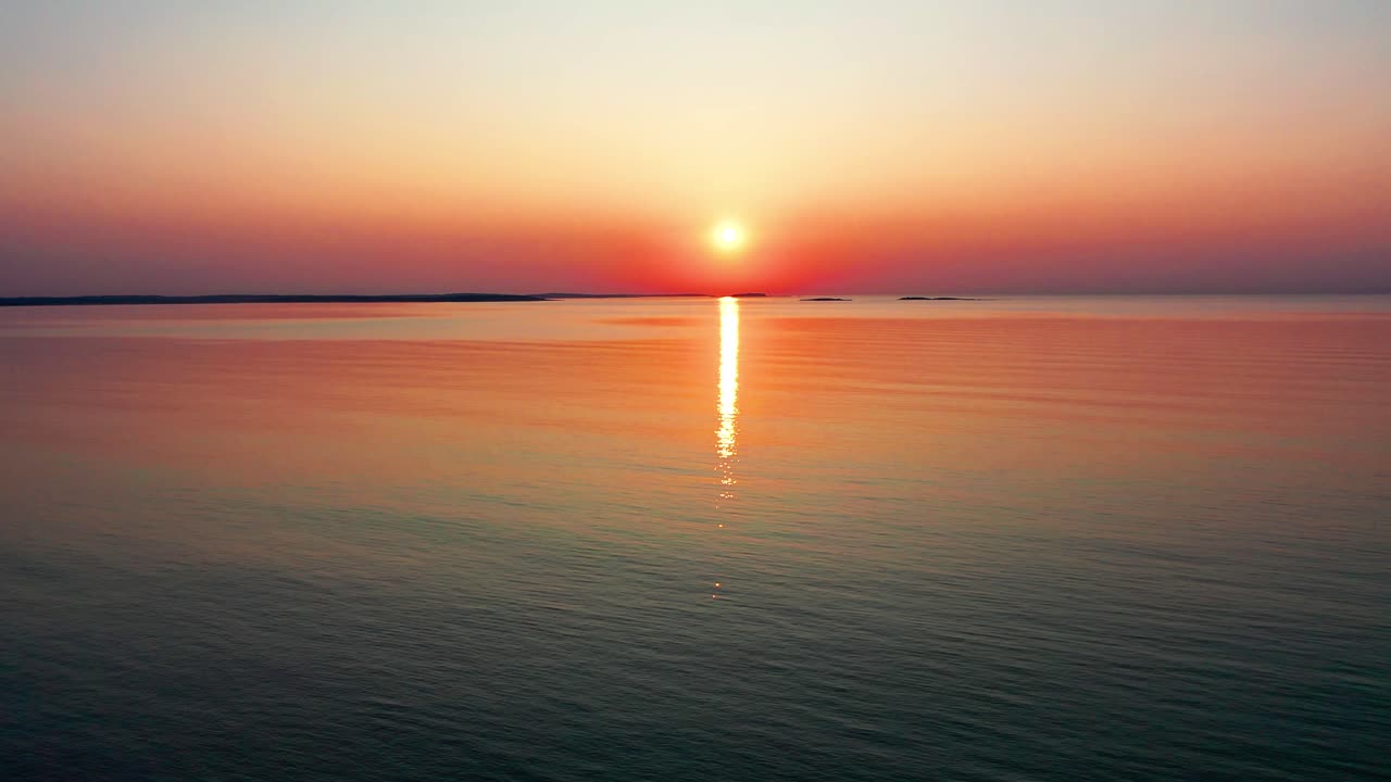 바다의 아름다운 일몰과 밝은 빛나는 태양은 바다의 평화로운 물결 위에 다채로운 빨간색, 오렌지색, 보라색 및 노란색 반사를 던집니다.