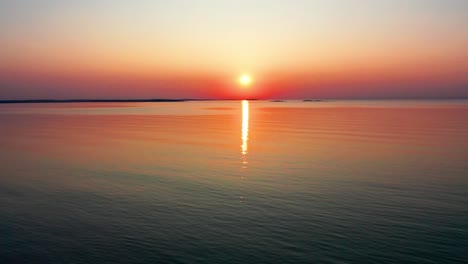 Hermosa-Puesta-De-Sol-En-El-Océano-Con-Un-Sol-Brillante-Que-Proyecta-Coloridos-Reflejos-Rojos,-Naranjas,-Morados-Y-Amarillos-Sobre-Las-Tranquilas-Olas-Del-Mar.