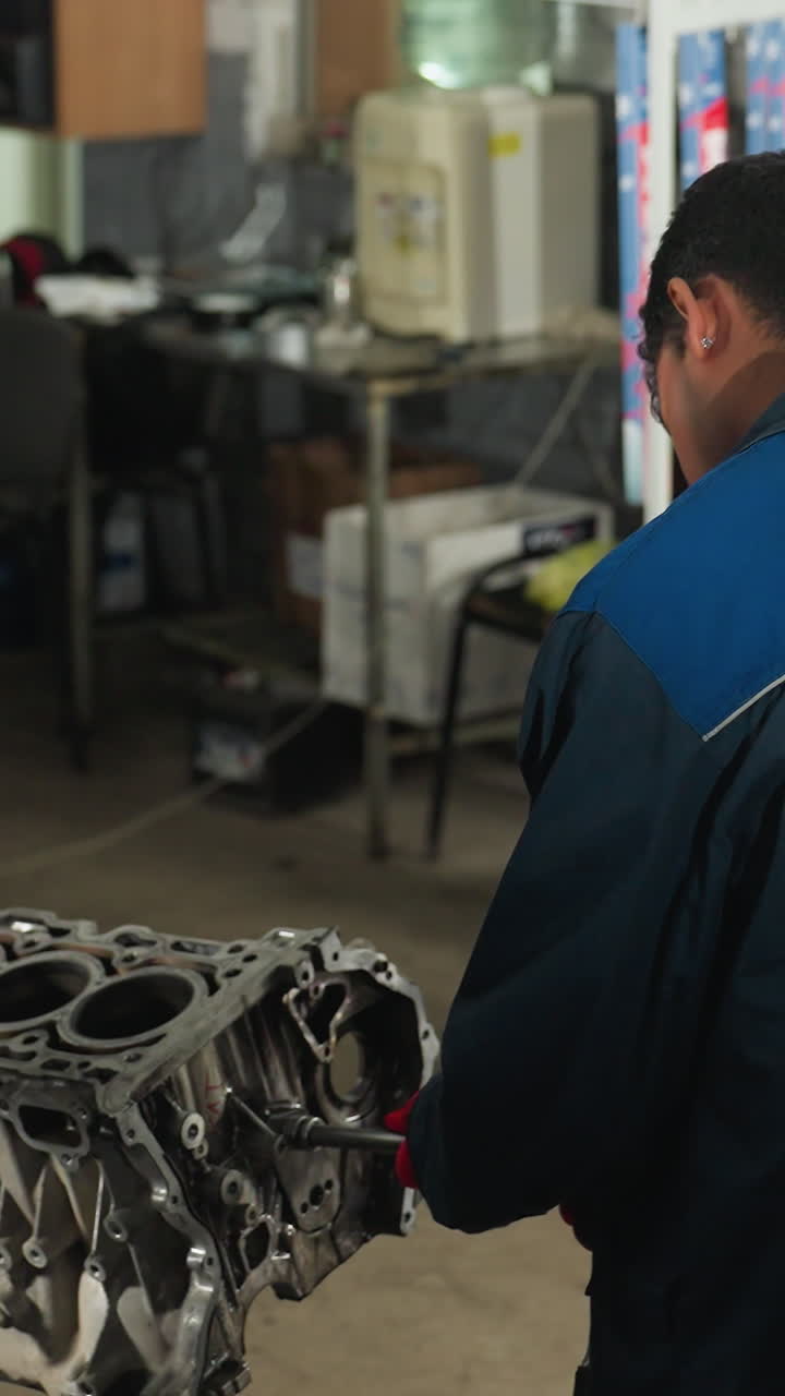 ingenieros automotores en un taller, uno se centró en el ensamblaje de un motor mientras su colega utiliza un teléfono inteligente, en medio de equipos mecánicos en el fondo