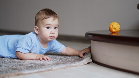 cute child lies on belly on the carpet. baby crawls up to the stair to get the toy. blurred background.