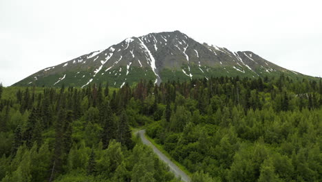 Dramatic-aerial-footage-of-snow-capped-mountain-rising-above-trees-in-Alaska