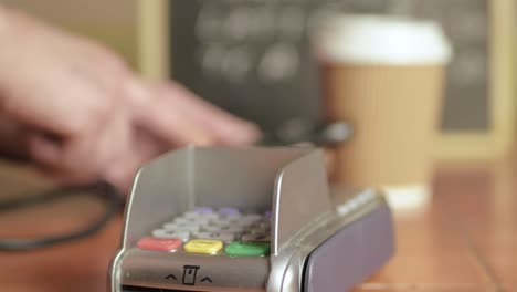 manos usando teléfono celular en la cafetería con terminal de pago cerca de la máquina