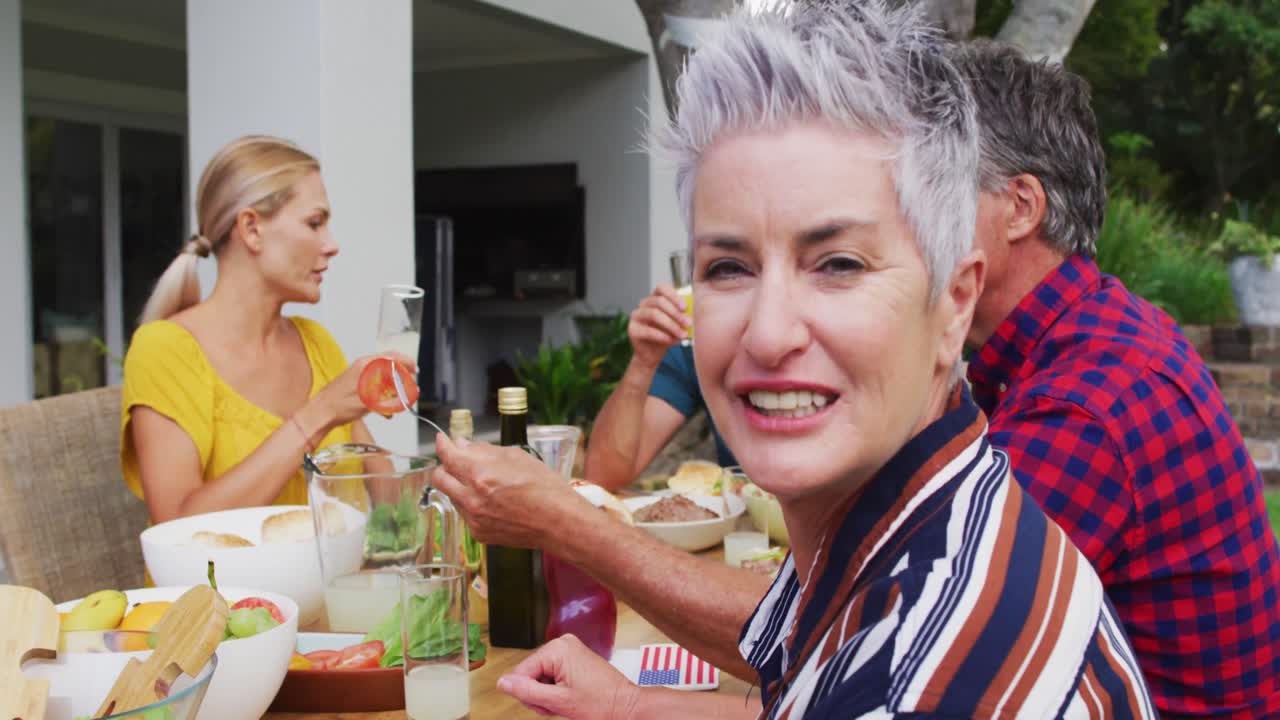 mujer mayor caucásica girando y sonriendo durante la comida de celebración familiar en el jardín