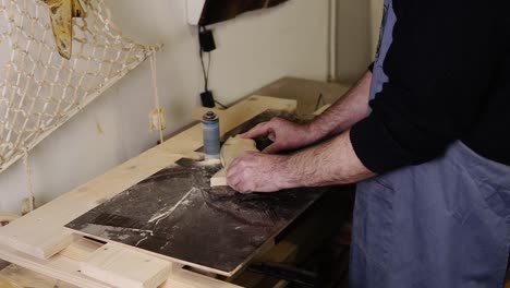 Man-grinds-the-fish-tail-shape-pattern-with-grinding-machine-with-sawdust-flying-into-the-sides,-profession,-carpentry-concept.-Side-view-of-a-man-sanding-wood-at-the-workshop.-Slow-motion