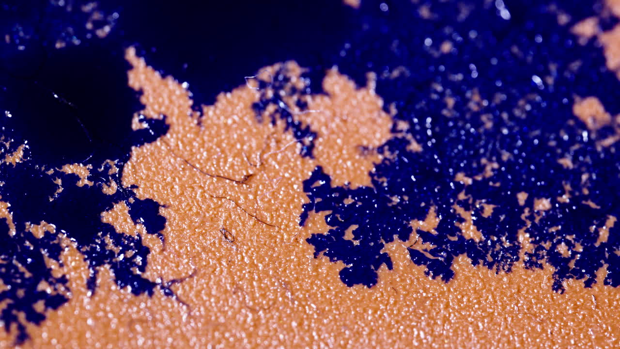 Vibrant orange and purple liquid textures blend and spread in an abstract macro close-up shot