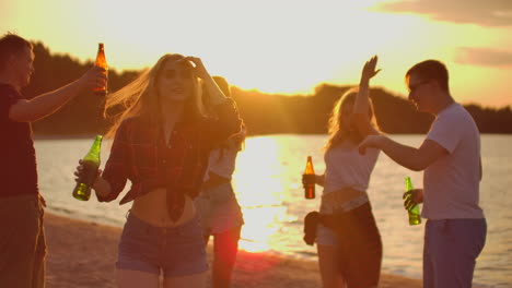 la joven con el cabello rubio está bailando con una figura delgada en la fiesta al aire libre con cerveza. ella gira en el baile a la música y disfrutando de la fiesta en la playa con los mejores amigos de buen humor.