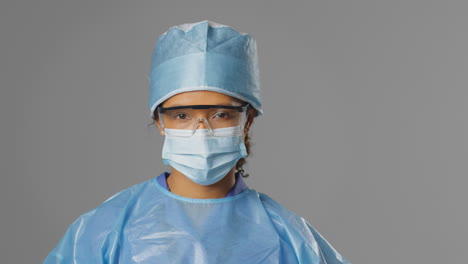 portrait of serious female surgeon wearing safety glasses and face mask against grey background