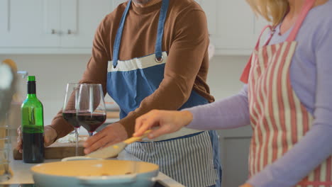 mature couple wearing aprons drinking red wine as they prepare ingredients and cook meal at home together - shot in slow motion