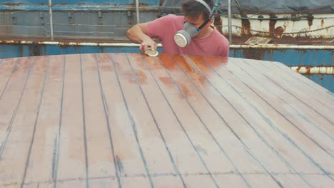 man manually sanding wooden boat cabin roof planks