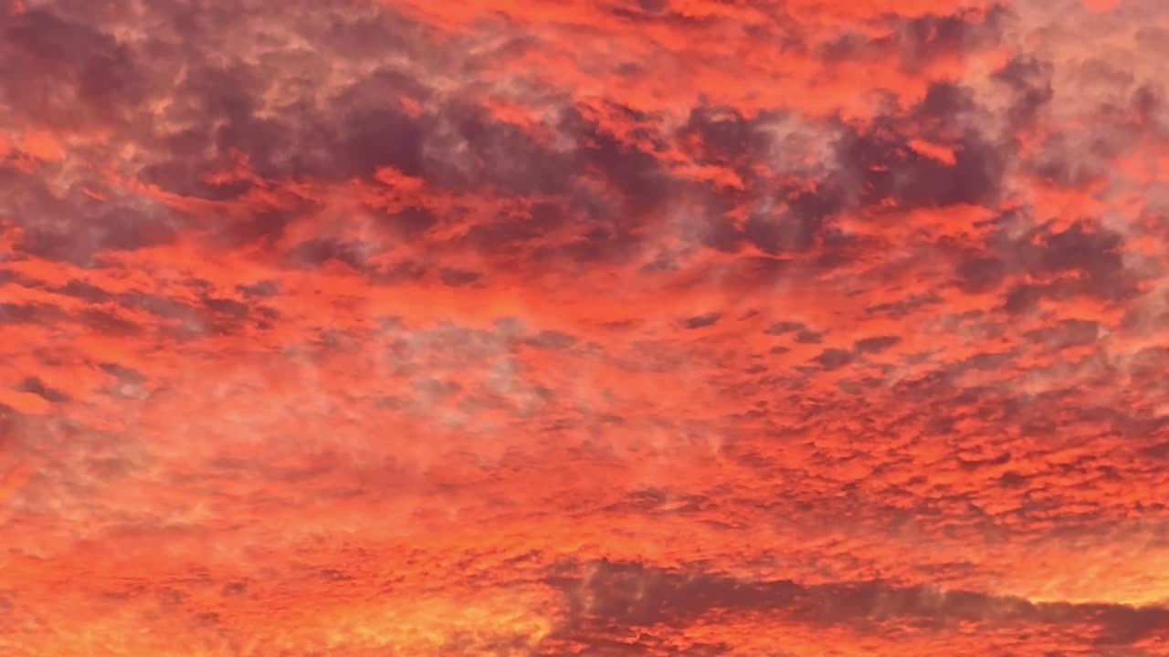 Fixed shot of vibrant red and orange sunset clouds filling the sky, showing dense textured cloud layers illuminated by golden light