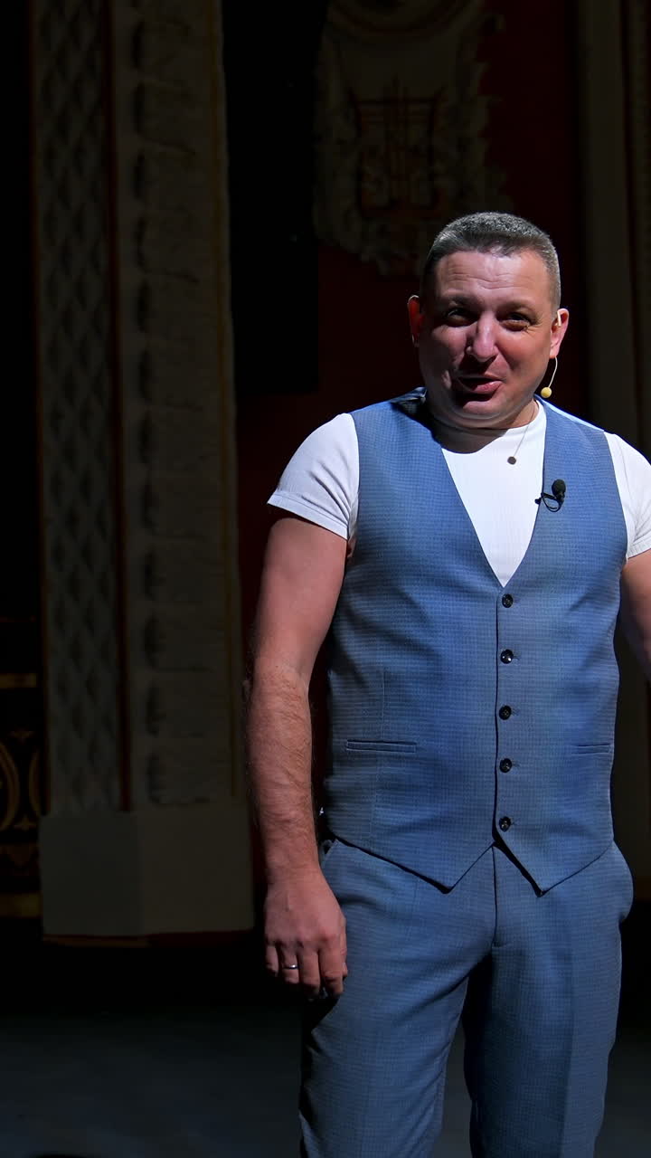 Showman entertains the audience under the light, front view. Big stage. Funny performer speaks to the camera. Active gestures on a stage. Vertical video