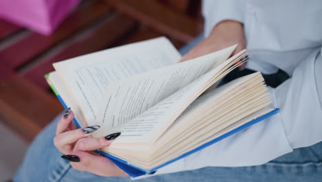 close-up of young adult flipping to another page of book while wearing denim and white shirt, black polished nails contrast with crisp pages