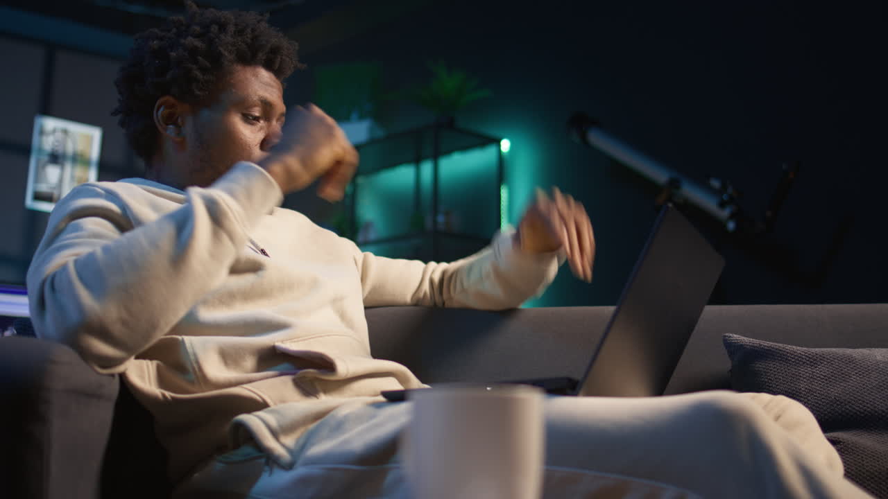 African american man suffering from a migraine and illness, sitting on couch at home and feeling overworked. Concerned young adult struggling with pain, tired and anxious guy. Camera A.