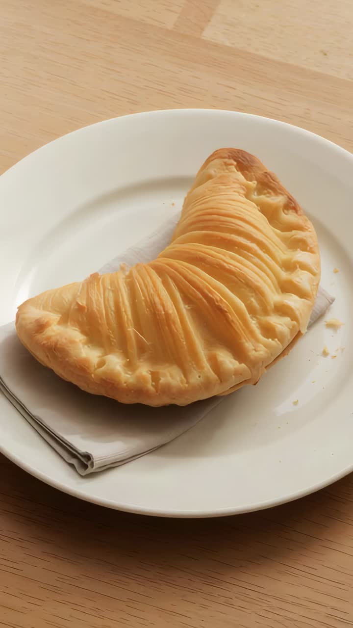Video verticale: ripresa che inizia con una panoramica verso l'alto mettendo in risalto un croissant su un piatto con delle briciole
