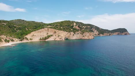 Vista-Aérea-Circular,-Playa-Aislada-Y-Vacía-Con-Arena-Blanca,-Agua-Turquesa,-Vegetación-Exuberante-Y-Pájaros-Volando,-Playa-Fari,-Isla-Thassos,-Grecia