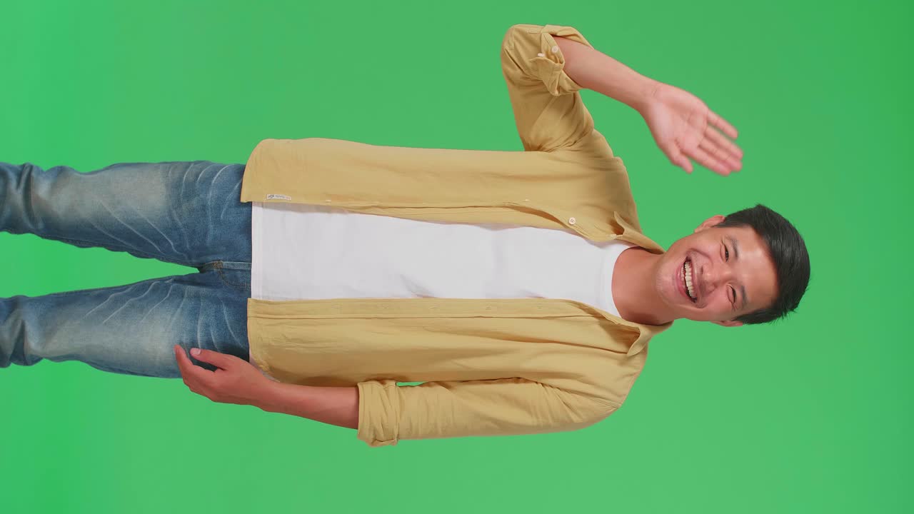 The Happy Young Asian Man Waving Hand And Say Bye Bye While Standing On Green Screen In The Studio