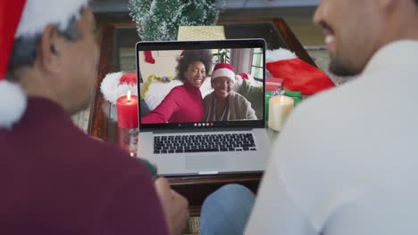 Smiling-biracial-father-and-son-using-laptop-for-christmas-video-call-with-family-on-screen