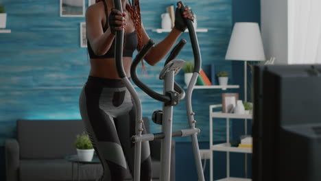 black athletic woman doing cardio training on elliptical bike in living room