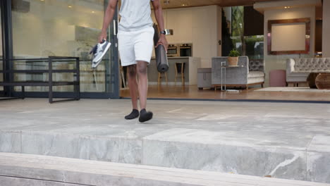carrying yoga mat, water bottle, african american man stepping down from patio at home, copy space