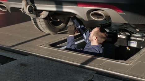 mechanic inspecting car undercarriage in service pit