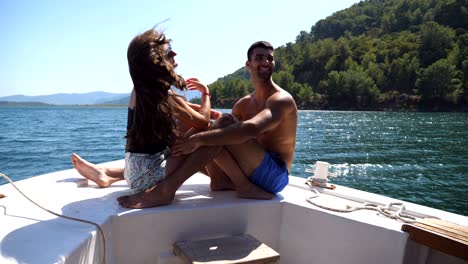 young pair sitting on bow of boat and posing to photographer at sunny day. happy couple in love spending time together on deck of ship and enjoying summer travel. concept of vacation or holiday. close up