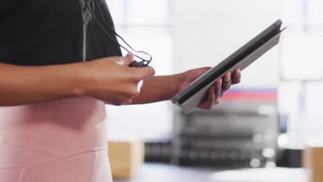 video de la sección media de una entrenadora de fitness afroamericana usando un cronómetro y una tableta en un gimnasio