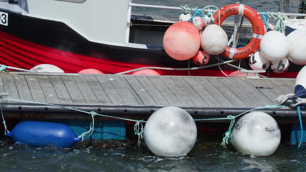Red fishing boat and dock with marine buoys, gentle water movement, natural daylight, stable camera
