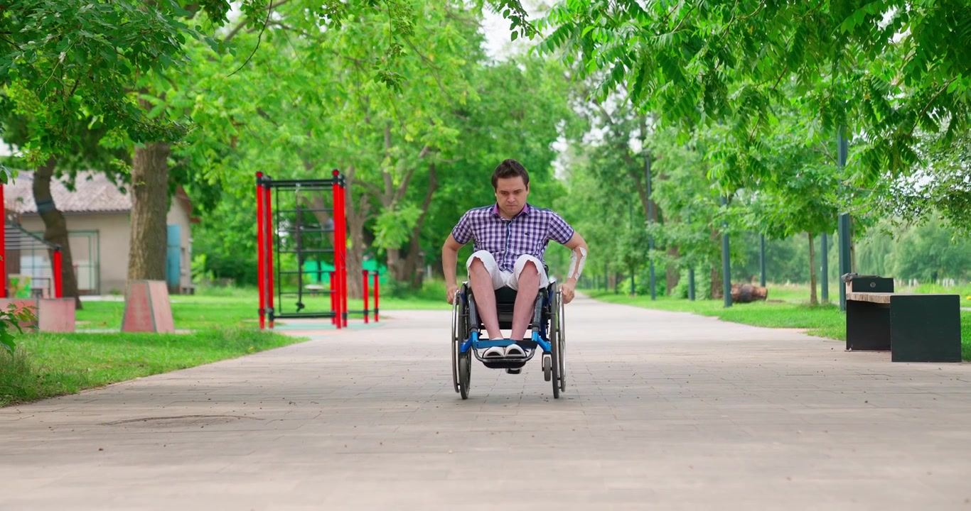Determined Young Man Pushing Wheelchair on Park Path