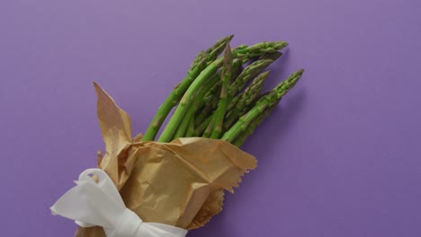 video of fresh asparagus wrapped with white ribbon and copy space over lilac background