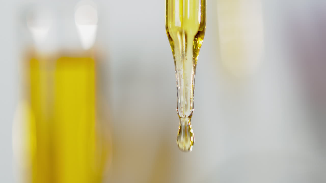 A yellow liquid flowing from a pipette, close shot