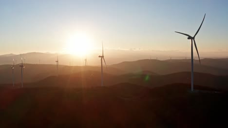 spinning wind turbines backlit by yellow orb of sunset, static aerial