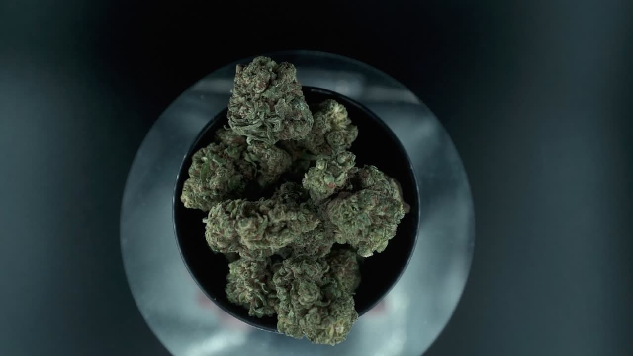 Grayish Green Dried Marijuana Buds view from above, pile of dried marijuana plants in a shiny bowl, trichomes strains, on a reflecting rotating stand, studio lights, slow motion 120 fps zoom out