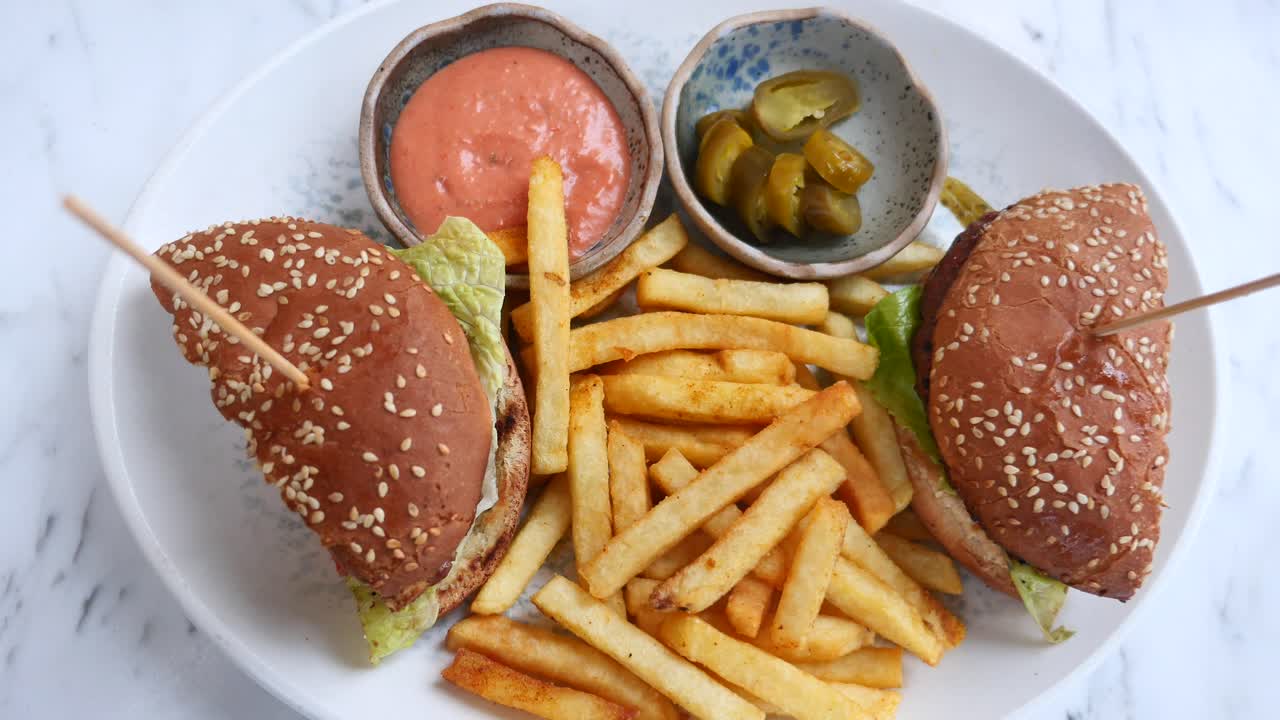 Two burgers with french fries, sauce, and pickled jalapenos on a plate