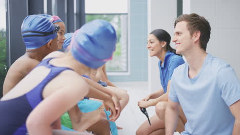 male and female coaches giving children in swimming class briefing as they sit on edge of pool