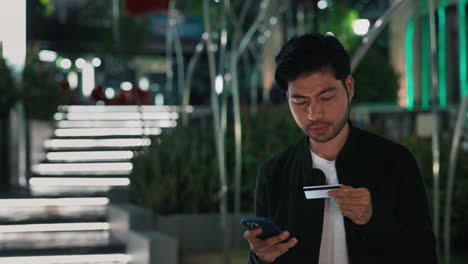 man using smartphone and credit card outdoors at night