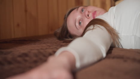 close up of girl lying on bed, feeling texture of material, looking thoughtfully, exploring sensory experience, indoor setting with natural wood background, reflecting on her thoughts