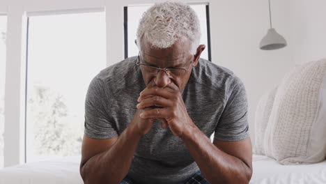 depressed senior man looking unhappy sitting on side of bed at home